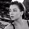 Black and white close-up portrait of a young woman looking to the side with wet hair against a rocky background.